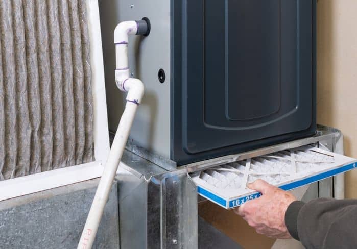Technician sliding a clean 16x25 furnace filter into a high-efficiency gas furnace during a maintenance visit